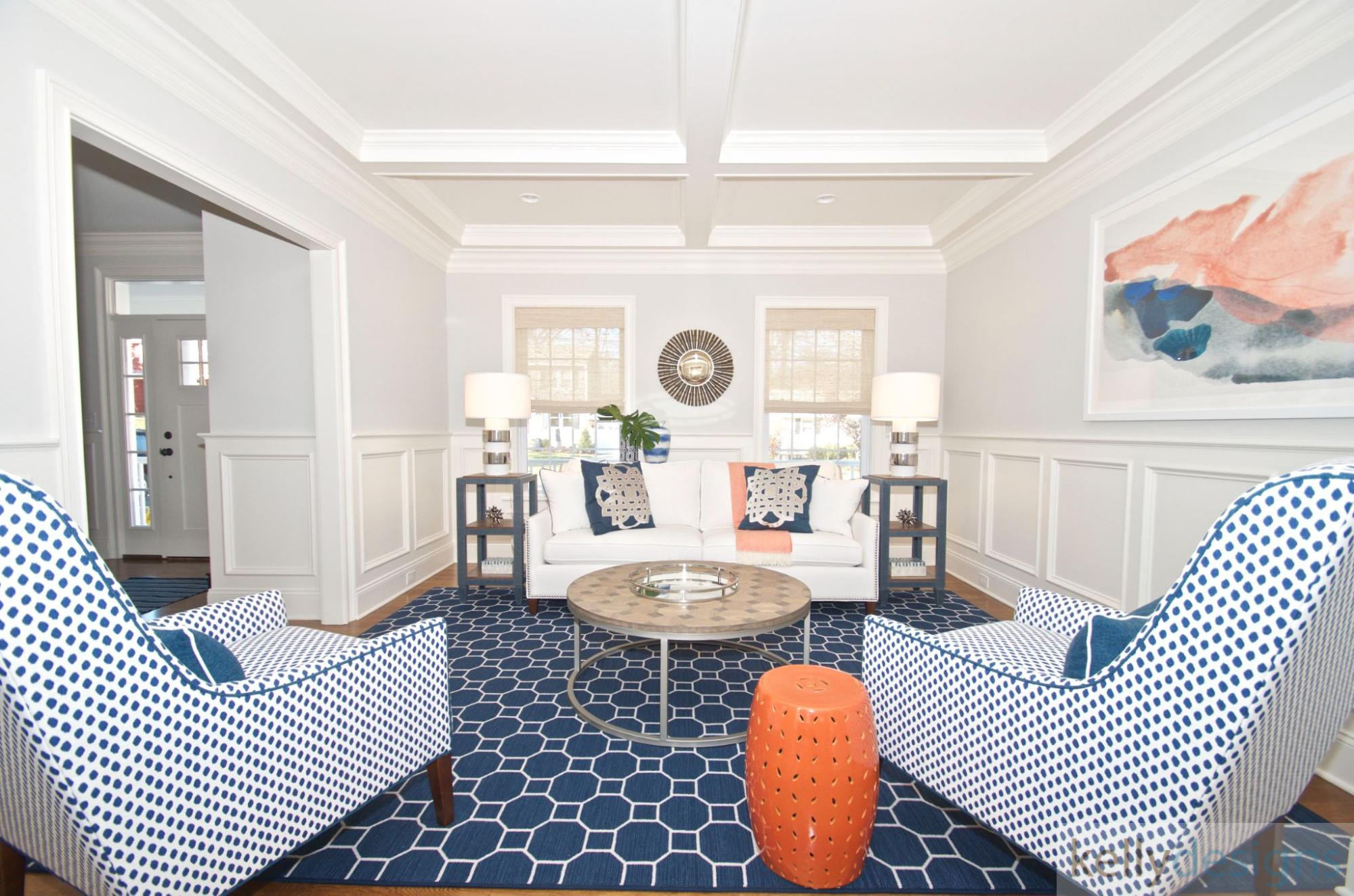 A cozy master bedroom with a blue patterned rug, white bedding on a dark wood bed frame, and two bedside tables with white lamps against a light gray wall.