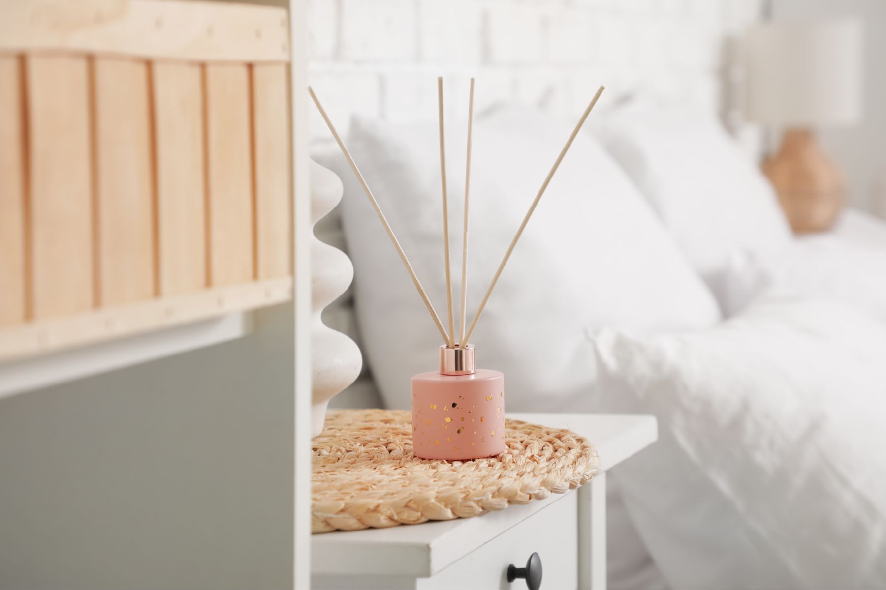 hite ceramic reed diffuser on a wooden nightstand in a bright, modern bedroom.
