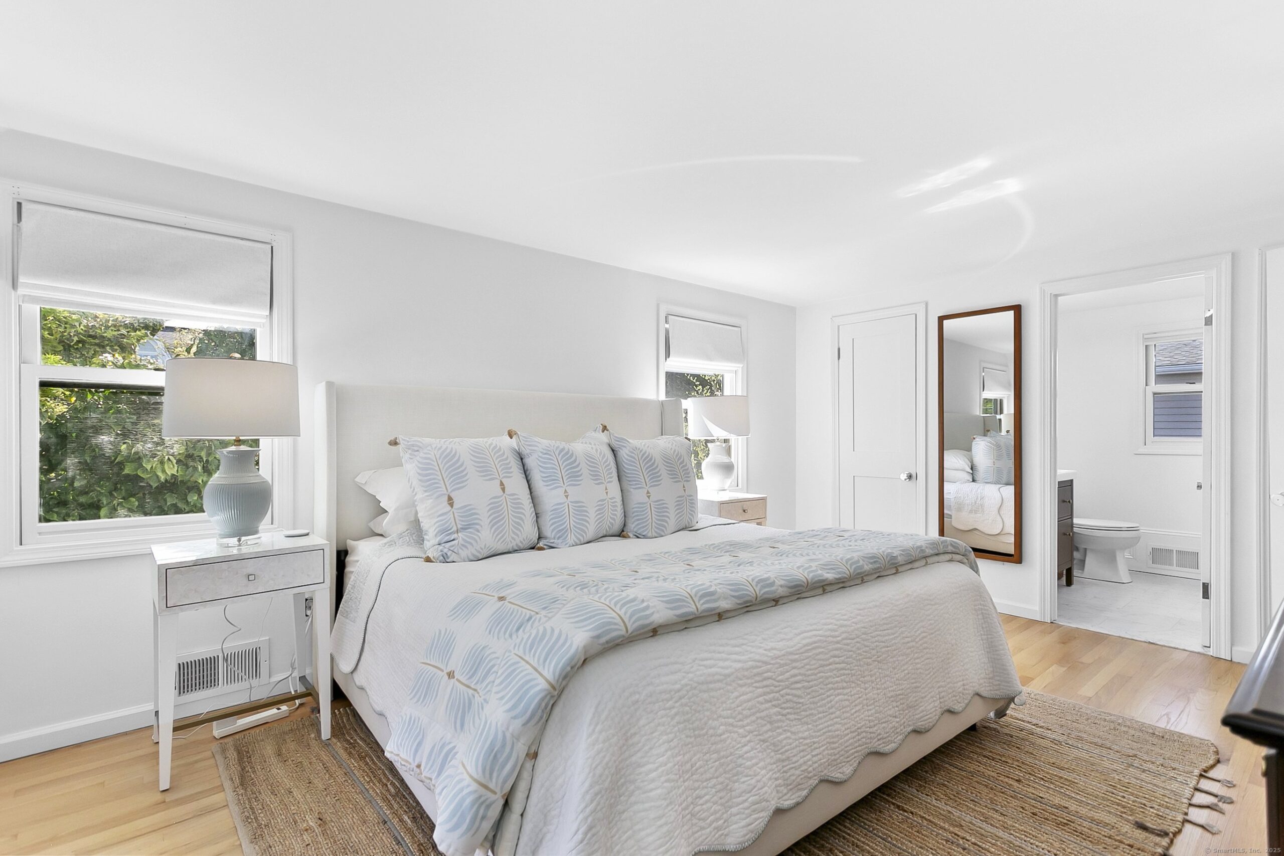 Symmetrical master bedroom design featuring matching wooden nightstands, identical glass lamps, and a neutral upholstered bed.