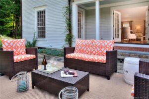 Wicker outdoor seating set with orange patterned cushions on a neutral area rug.