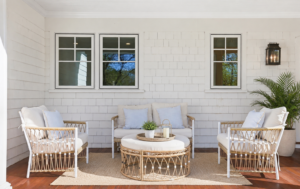 Coastal-style covered porch in Fairfield County with white shingle siding, woven outdoor furniture, light blue cushions, and a black lantern sconce.