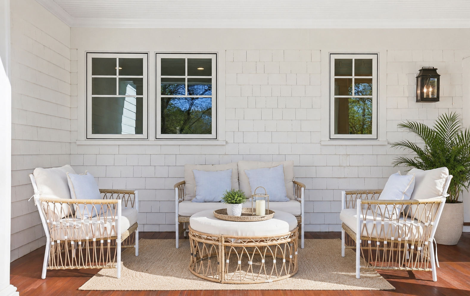 Coastal-style covered porch in Fairfield County with white shingle siding, woven outdoor furniture, light blue cushions, and a black lantern sconce.